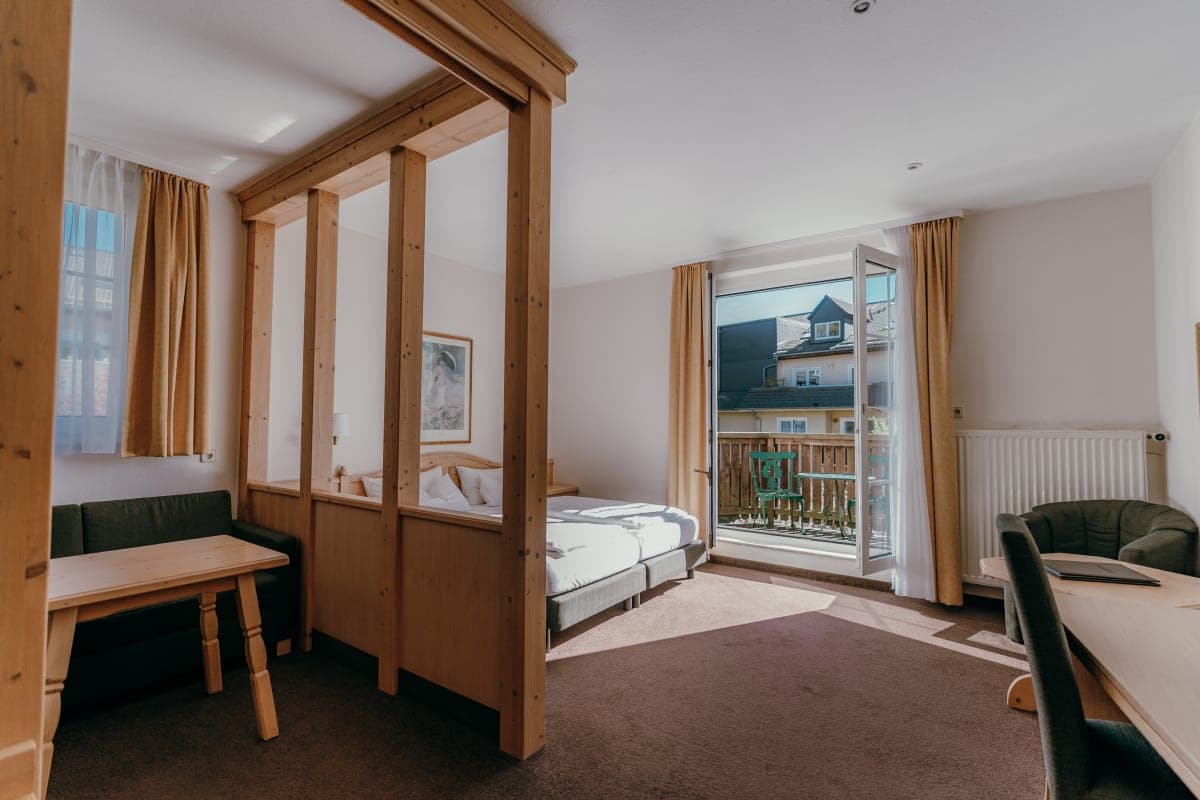 Chambre lumineuse avec lit à baldaquin en bois et balcon au Sonnenhotel Hoher Hahn