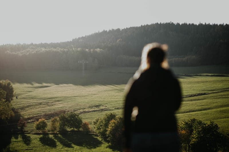 Člověk hledící na mlhou zahalené kopce a lesy ve zlatavém ranním světle