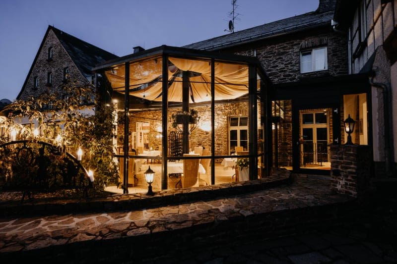 Vue extérieure de l'Hôtel Hoher Hahn la nuit, avec son jardin d'hiver vitré illuminé et sa façade historique en ardoise