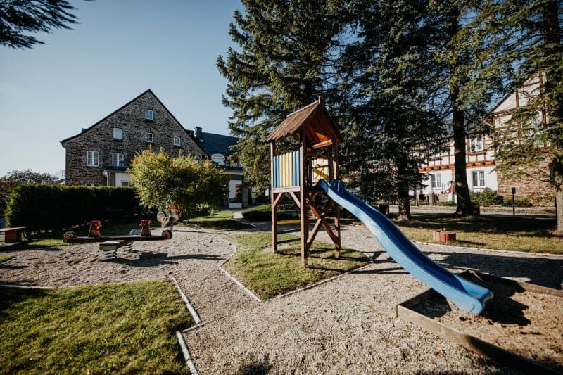 Children's playground with a blue slide and rocking animals in the sunny hotel garden in front of a historic stone building