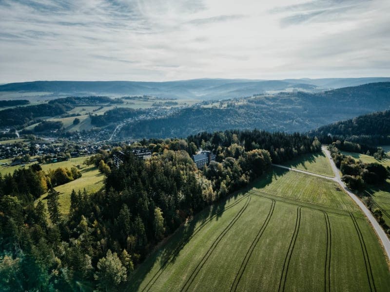 Aerial view of the Hoher Hahn hotel surrounded by green meadows and the Thuringian forest landscape with hills in the background