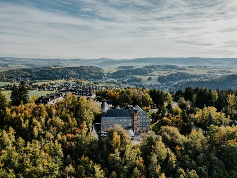 Vista aérea del Hotel Hoher Hahn rodeado de bosque mixto otoñal en el Erzgebirge