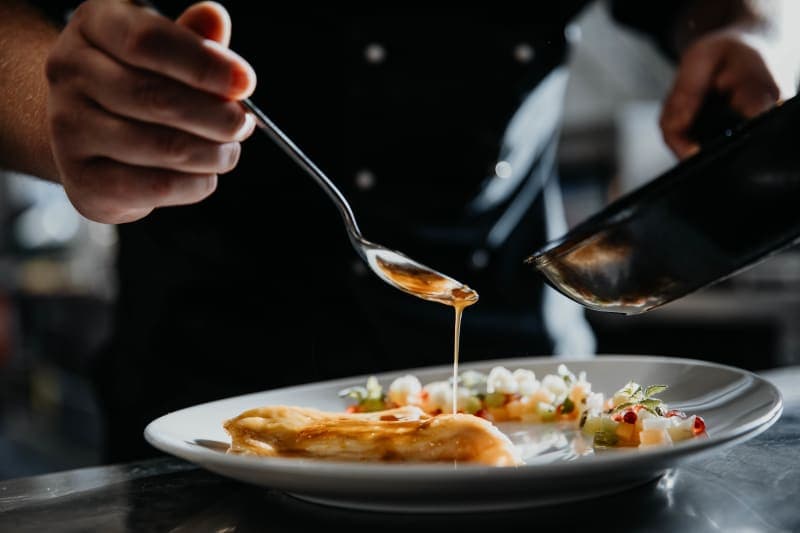 Chef spooning a golden sauce over an elegantly plated dish on a white plate