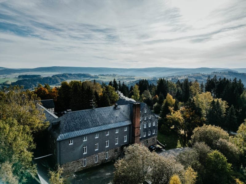 Letecký pohled na hotel Hoher Hahn obklopený podzimním lesem a ranní mlhou