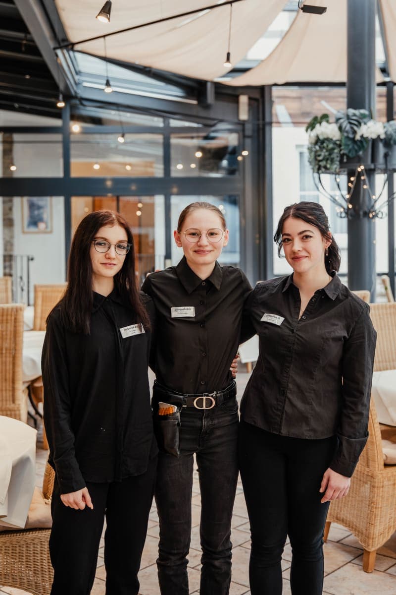 Tres empleadas de servicio sonrientes con uniforme negro en el restaurante del hotel Hoher Hahn